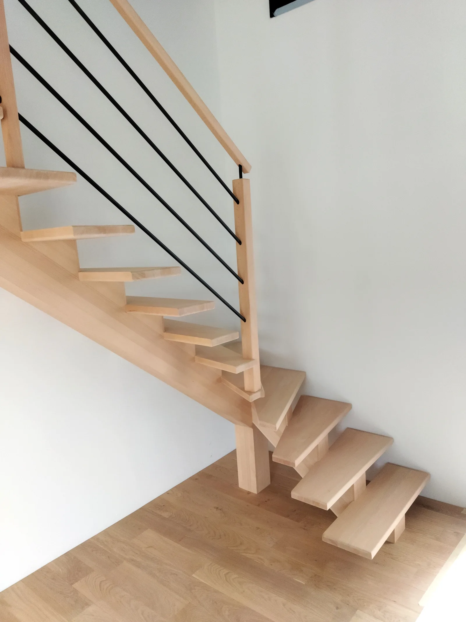 Escalier quart tournant bas limon central en hêtre, rampe Croisière barreaux noirs, intérieur contemporain posé par HALLOU ESCALIERS, à Dinard (35). Fabricant d'escaliers sur mesure