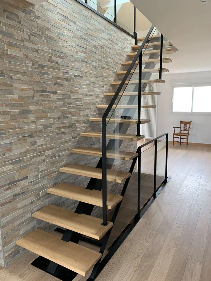 Escalier métal droit limon Paquebot en acier noir thermolaqué, marches en chêne massif, garde-corps verre feuilleté au palier, posé contre un mur en parement ardoise dans une maison contemporaine à Betton (35). — HALLOU ESCALIERS, Betton (35).